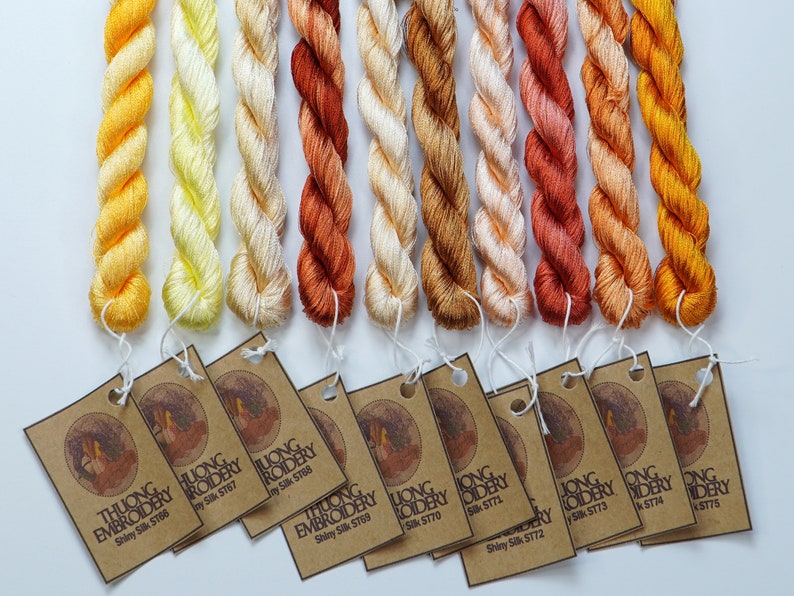 May include: Ten spools of embroidery floss in shades of yellow, orange, and red. Each spool has a brown paper tag with the text "THUONG EMBROIDERY Shiny Silk" and a corresponding number.