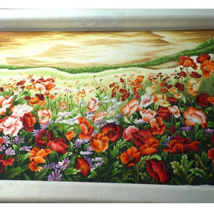 May include: A close-up of a needlepoint embroidery depicting a field of red, orange, and white poppies with green leaves and stems. The background is a soft yellow and brown, suggesting a sunset or sunrise.