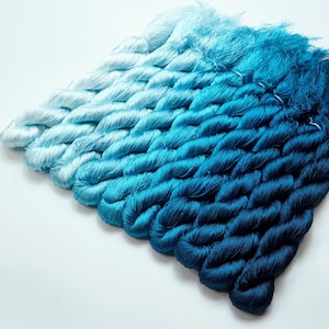 Könnte beinhalten: Eine Sammlung von blauen Seiden-Stickgarn-Spulen, die in einem Farbverlauf von Hellblau bis Dunkelblau angeordnet sind.