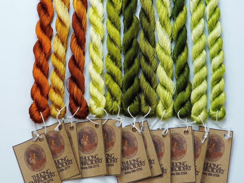 May include: A set of 10 spools of embroidery floss in shades of orange, yellow, and green. The floss is labeled "THUONG EMBROIDERY" and has a silk sheen.