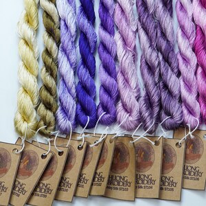 May include: Ten spools of embroidery floss in shades of purple, pink, and yellow. Each spool has a brown paper tag with the text "Luong Embroidery" and a unique product code.