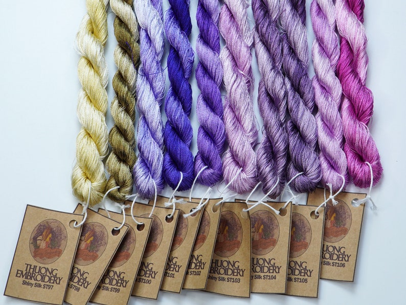 May include: Ten spools of embroidery floss in shades of purple, pink, and yellow. Each spool has a brown paper tag with the text "Luong Embroidery" and a unique product code.