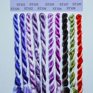 May include: Nine spools of embroidery floss in various shades of purple, green, black, and red. The spools are labeled with the numbers ST100 through ST109.