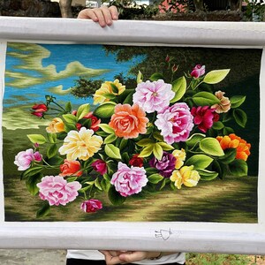 May include: A framed embroidery depicting a bouquet of colorful flowers, including pink, red, yellow, and orange roses, with green leaves and a blue sky background.