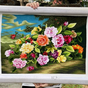 May include: A framed embroidery depicting a bouquet of colorful flowers, including pink, red, yellow, and orange roses, with green leaves and a blue sky background.
