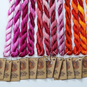 May include: A collection of 14 skeins of embroidery floss in shades of pink, red, orange, and yellow. Each skein is labeled with "THUONG EMBROIDERY" and a unique number.