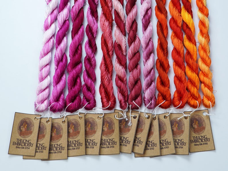May include: A collection of 14 skeins of embroidery floss in shades of pink, red, orange, and yellow. Each skein is labeled with "THUONG EMBROIDERY" and a unique number.