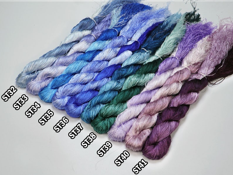 May include: A collection of 10 skeins of embroidery floss in various shades of blue, green, and purple. The skeins are labeled with the numbers ST32, ST33, ST34, ST35, ST36, ST37, ST38, ST39, ST40, and ST41.