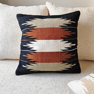 May include: A black, white, brown, and beige patterned throw pillow with a geometric design. The pillow is on a white couch.