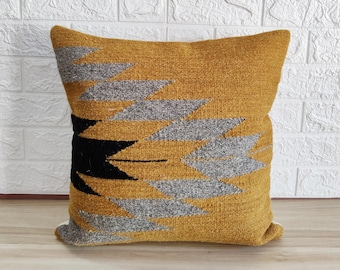 Puede incluir: Una almohada de tiro de color amarillo mostaza con un patrón geométrico en gris y negro. La almohada está hecha de una tela suave y texturizada.