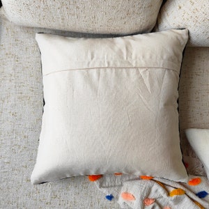 May include: A white cotton pillow with a black trim. The pillow is lying on a textured surface.