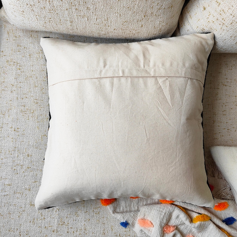 May include: A white cotton pillow with a black trim. The pillow is lying on a textured surface.