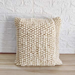 May include: A cream-colored throw pillow with a textured, bumpy surface. The pillow is made of a soft, fluffy material.