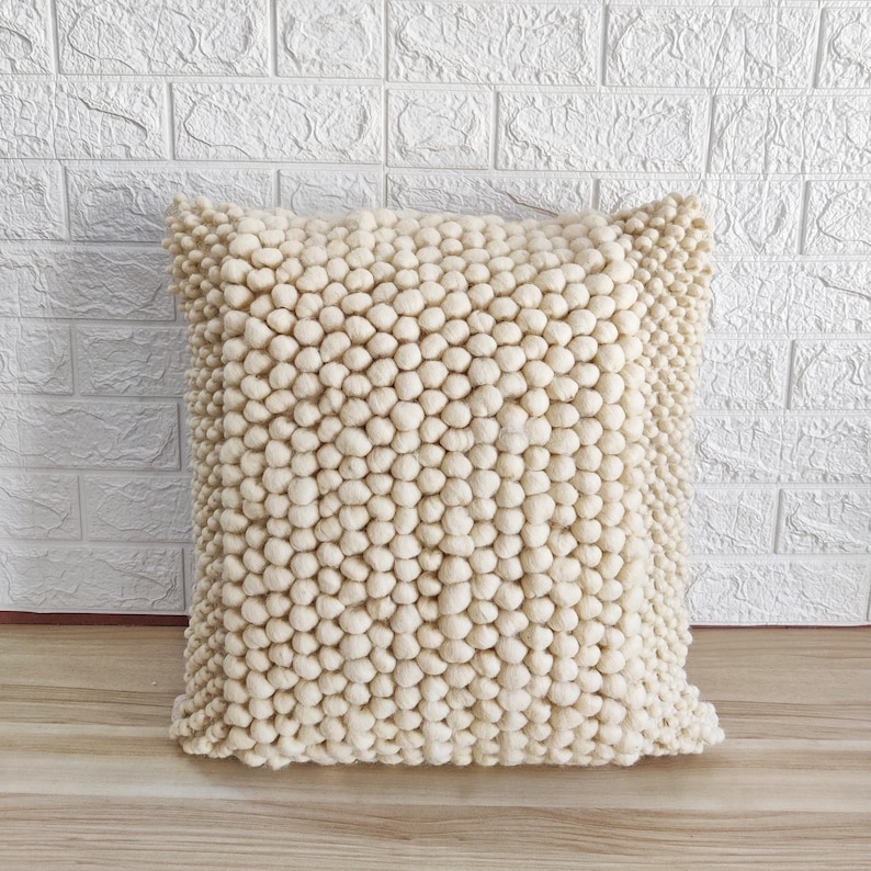 May include: A cream-colored throw pillow with a textured, bumpy surface. The pillow is made of a soft, fluffy material.