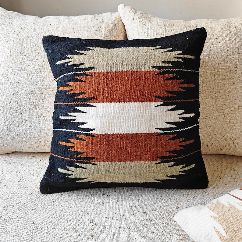 May include: A black, white, brown, and beige patterned throw pillow with a geometric design. The pillow is on a white couch.