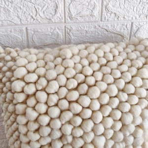 May include: A white fluffy pillow with a textured surface made of small, round balls. The pillow is soft and plush, perfect for adding a touch of comfort and style to any room.