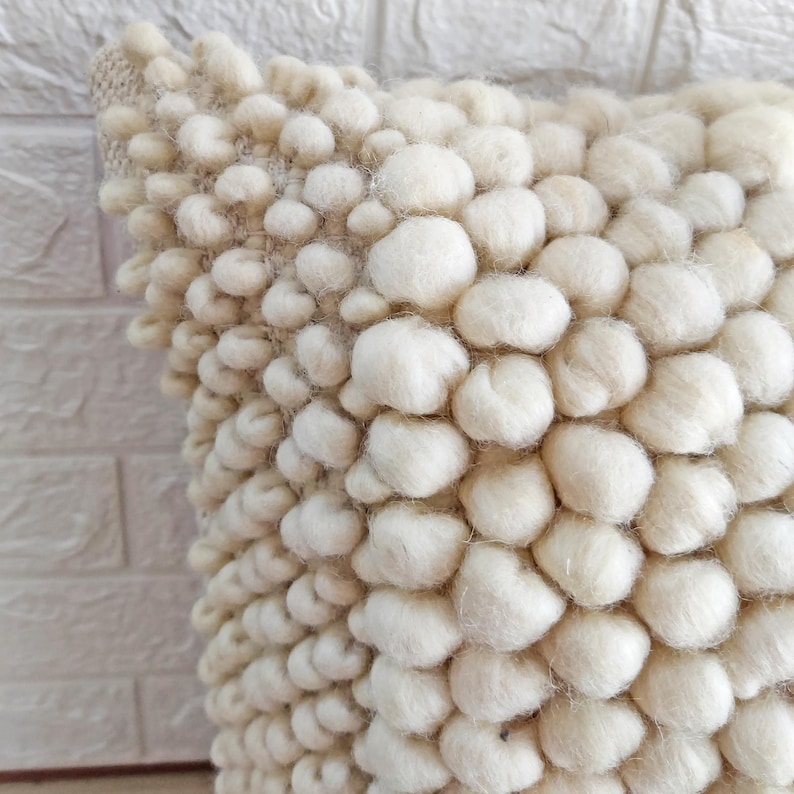 May include: A white, fluffy pillow with a textured surface made of small, round balls. The pillow is soft and plush, and would be a great addition to any living room or bedroom.