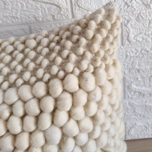 May include: A white throw pillow with a textured surface made of small, round, white pom-poms. The pillow is soft and fluffy, and would be a great addition to any living room or bedroom.