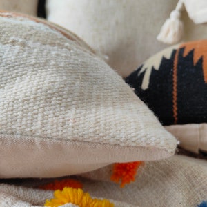 May include: Close-up of a white, textured throw pillow with a subtle woven pattern. The pillow is made of a soft, natural material and has a simple, elegant design.