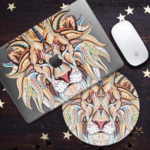 Puede incluir: Una piel de portátil colorida y estampada y una alfombrilla de ratón a juego que presenta la cara de un león. La cara del león está detallada con intrincados patrones y colores, incluyendo amarillo, naranja, azul y verde.
