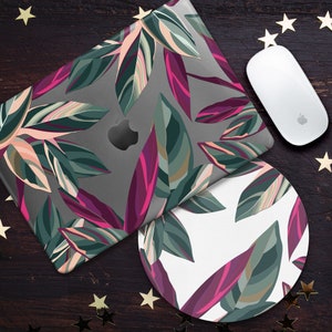 May include: A laptop and mouse mat set with a colourful botanical leaf pattern in green, pink, and white. The laptop has the Apple logo. The mouse is white. The set is on a dark wood surface with gold star decorations.