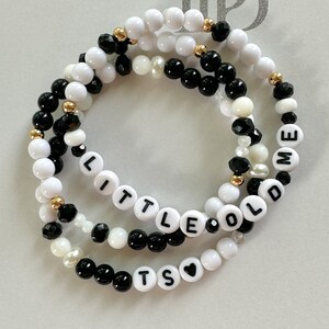 Peut inclure: Trois bracelets superposés avec des perles noires et blanches. Les perles épellent "Little Old Me" et "Its" avec un symbole de cœur.