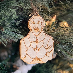 May include: A wooden Christmas ornament featuring a cartoon image of a man with a surprised expression. The ornament is painted in shades of brown and white.