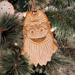 Può includere: Un ornamento natalizio in legno a forma di personaggio dei cartoni animati con una lunga barba e un ampio sorriso. L'ornamento è dipinto in tonalità di marrone e bianco.
