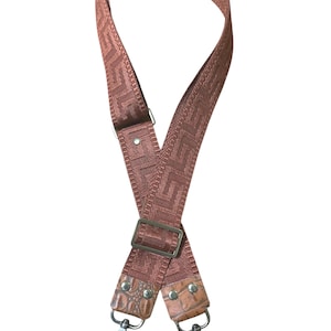 May include: A brown patterned bag strap with silver-tone metal hardware. The strap features a geometric design and crocodile-textured leather accents. Includes a decorative key charm.