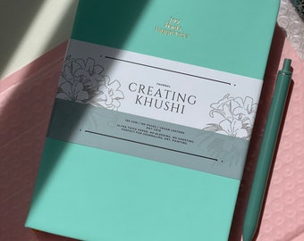 May include: A teal journal with the text "Joy What Happiness" and "Creating Khushi" on the cover. The journal is 180 pages, vegan leather, dot grid, ultra thick paper, no bleeding, no ghosting, perfect for journaling, art, painting.