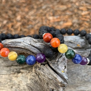 May include: Two bracelets with black lava rock beads and colorful gemstone beads. The beads are arranged in a rainbow pattern.