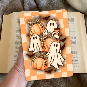 Op de afbeelding: Een rechthoekige kaart met Halloween-thema met cartoongeesten, pompoenen en vleermuizen. De geesten zijn wit met zwarte ogen en strikken, die een koffiekopje vasthouden. De pompoenen zijn oranje met geruite strikken. De achtergrond is oranje en wit geblokt.