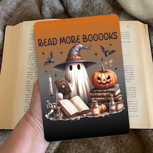 Op de afbeelding: Een Halloween-thema boekomslag met een spook met een heksenhoed, een boek vasthoudend, omringd door pompoenen, vleermuizen en de tekst "READ MORE BOOOOKS". De achtergrond heeft een oranje en grijze gradiënt.