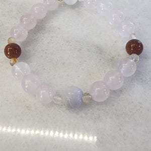 Puede incluir: Un brazalete de cuentas rosadas y blancas con una piedra azul claro y cuentas marrones.