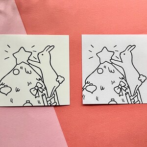 May include: Two black and white illustrations of bunnies decorating a Christmas tree. One bunny is placing a star on top of the tree, while the other bunny is holding a ribbon.