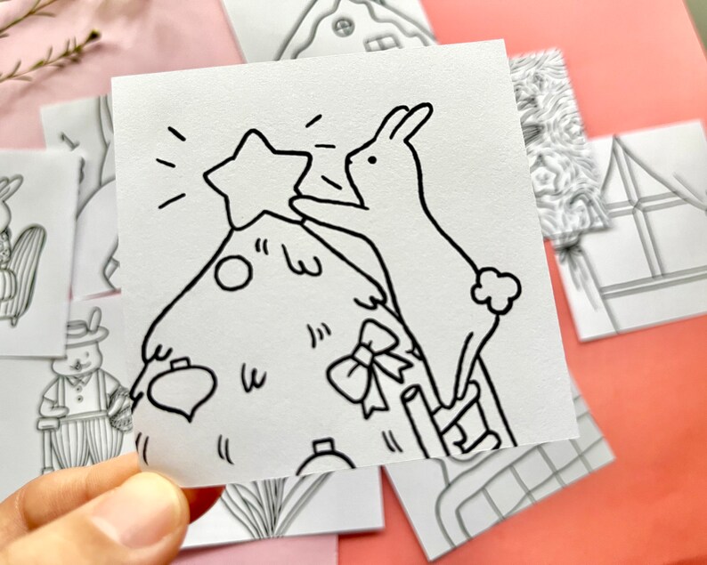 May include: A black and white line drawing of a rabbit placing a star on top of a Christmas tree. The rabbit is standing on a ladder and the tree is decorated with baubles and a bow.