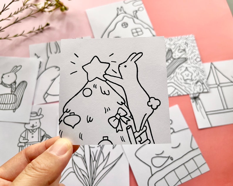 May include: A black and white line drawing of a rabbit decorating a Christmas tree with a star on top. The rabbit is standing on a ladder.