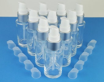 Könnte beinhalten: Ein Set aus zehn durchsichtigen Glasflaschen mit silbernen Pumpenköpfen und weißen Kappen. Die Flaschen sind in einem Kreis auf einer blauen Oberfläche angeordnet. Auf der Oberfläche befinden sich auch zehn durchsichtige Plastikkappen.