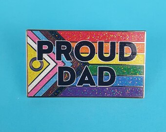 May include: A rainbow glitter enamel pin with the text "PROUD DAD" in black letters. The pin features a rainbow flag design with a gender-inclusive symbol.
