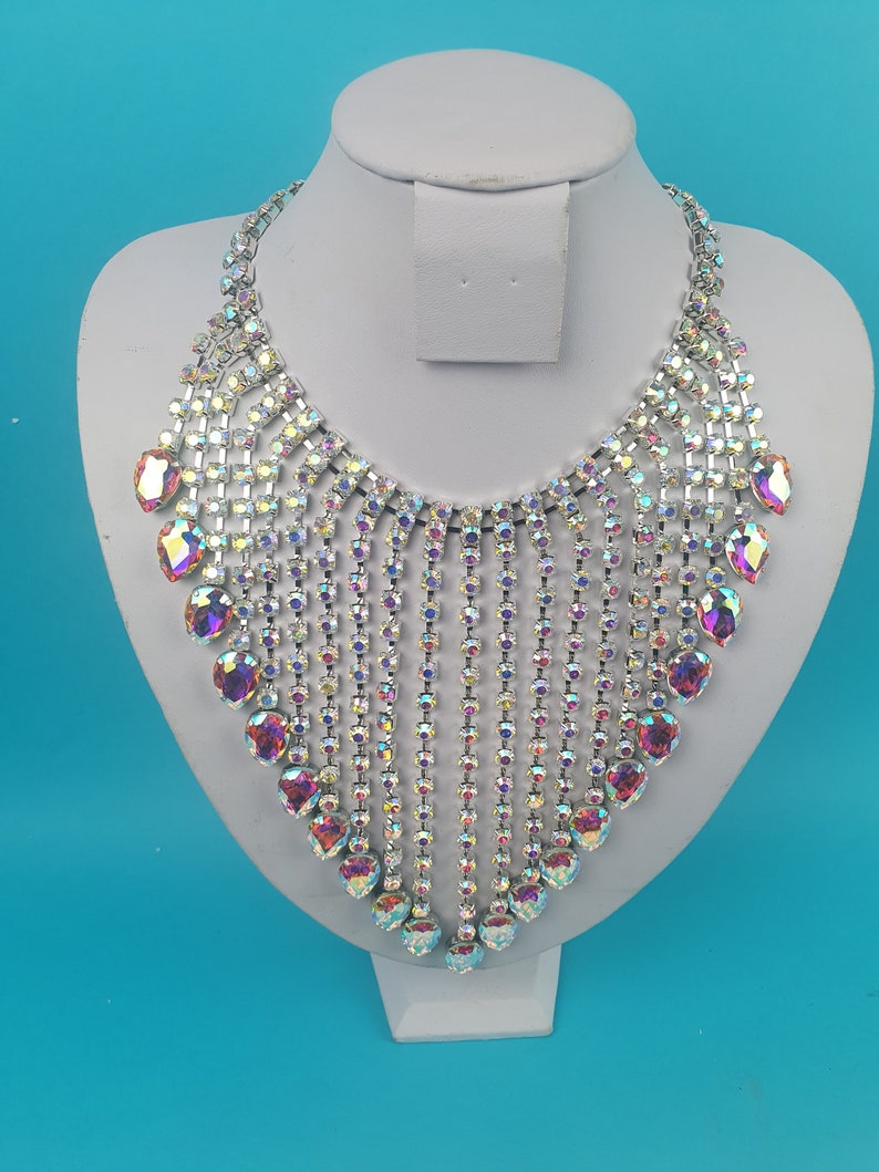 May include: A silver necklace featuring iridescent crystal stones. The necklace has a cascading design with multiple rows of stones.