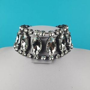 May include: A silver rhinestone choker necklace with a row of large, clear, marquise-shaped rhinestones. The necklace is on a white mannequin bust.