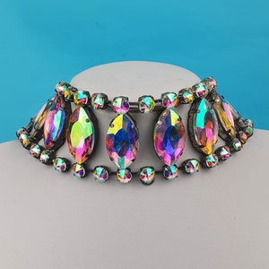 May include: A multi-colored iridescent crystal choker necklace with a silver chain and oval-shaped crystals.