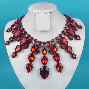 May include: A red crystal necklace with a teardrop design. The necklace is made of many small crystals that are connected together to form a long, flowing chain. The necklace is perfect for adding a touch of sparkle to any outfit.