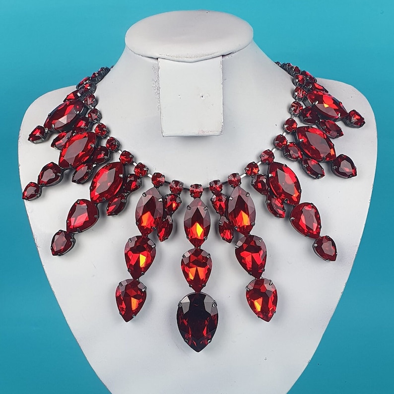 May include: A red crystal necklace with a teardrop design. The necklace is made of many small crystals that are connected together to form a long, flowing chain. The necklace is perfect for adding a touch of sparkle to any outfit.