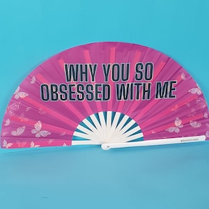 Può includere: Un ventaglio rosa con manico bianco e disegni di farfalle. Il ventaglio ha la scritta "WHY YOU SO OBSESSED WITH ME" stampata su di esso.