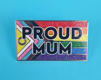 May include: A rainbow glitter enamel pin with the text "PROUD MUM" in black letters. The pin features a rainbow flag design with a gender symbol.