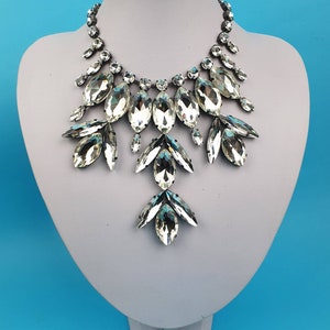 Pode incluir: Um colar de declara&ccedil;&atilde;o prateado com grandes cristais transparentes facetados dispostos em um design floral em cascata.