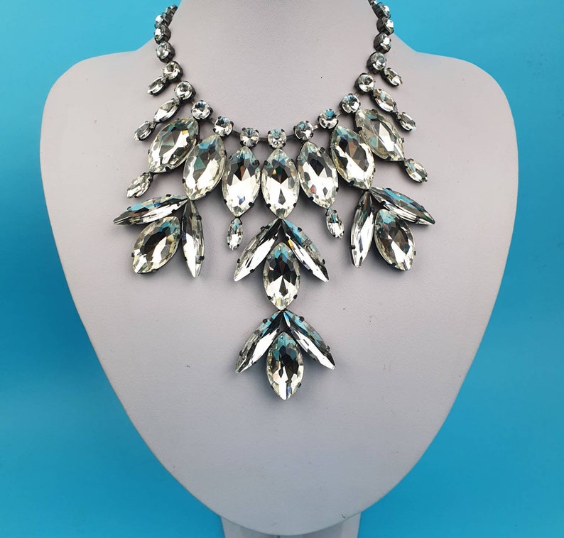 Pode incluir: Um colar de declara&ccedil;&atilde;o prateado com grandes cristais transparentes facetados dispostos em um design floral em cascata.
