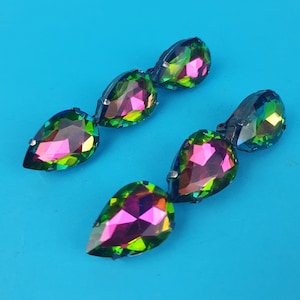 May include: A pair of iridescent teardrop-shaped earrings with a black metal setting. The earrings are made of faceted glass and have a rainbow of colors, including green, pink, and purple.