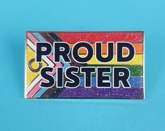 May include: A rainbow glitter enamel pin with the text "PROUD SISTER" in black letters.